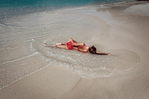 Prachtige roodharige vrouw met sexy lichaam gekleed in rode bikini en zonnebril liggend op het strand, verleidelijke vrouw in zwembroek rust na het zwemmen. Phuket. Thailand. Achteraanzicht