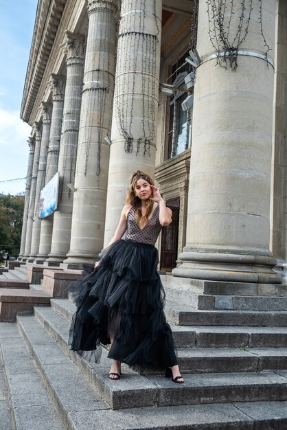 Prachtige sexy vrouw in een zwarte jurk, staande op de trap. Modern meisje op stadswandeling