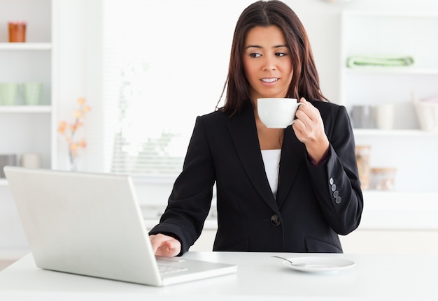 Prachtige vrouw in pak genieten van een kopje koffie terwijl u ontspant met haar laptop