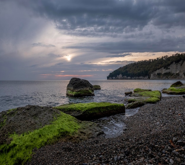 Prachtige zee in de herfst met epische zonsondergang met wolken en groene algenkeien.