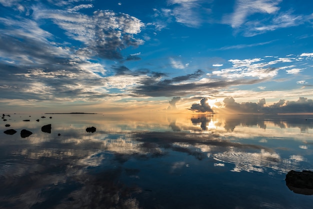 Prachtige zonsopgang, kleurrijke wolken die als een spiegel in de gladde zee reflecteren. Hatoma-eiland aan de horizon.