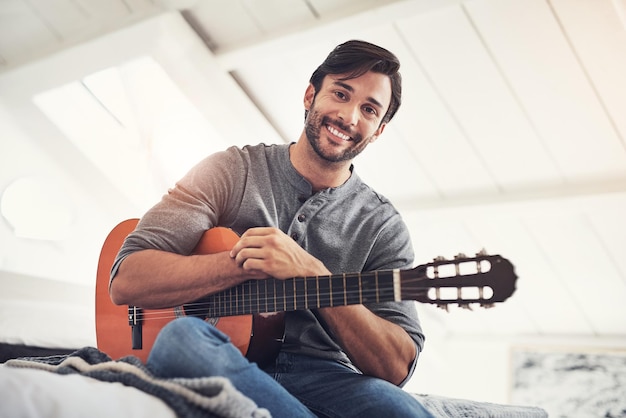 Практика делает совершенным Снимок красивого молодого человека, играющего на гитаре дома