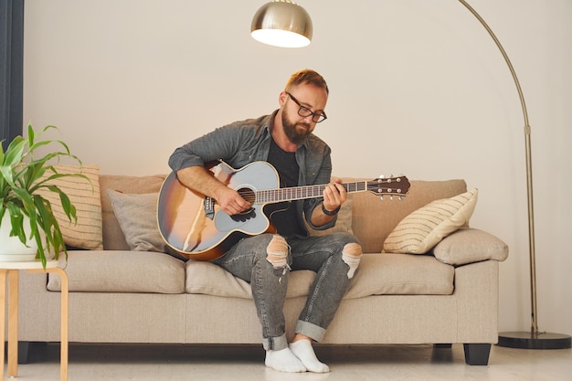 Practicing songwriting skill Man in casual clothes and with acoustic guitar is indoors