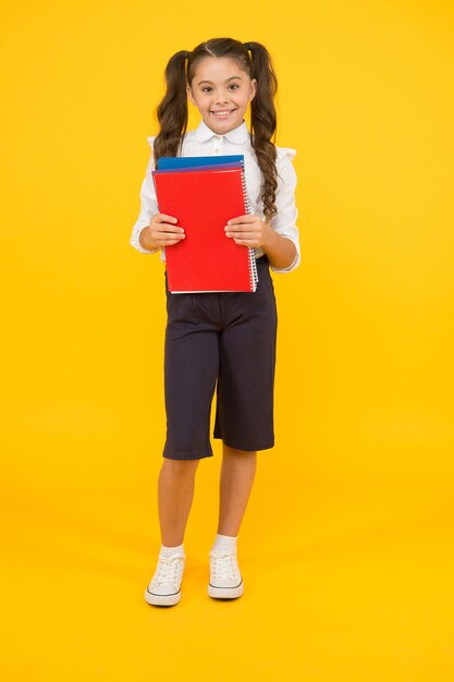 Practise your reading skills Cute small child holding reading books on yellow background Adorable little schoolgirl learn reading at primary school Improve your language understanding with reading