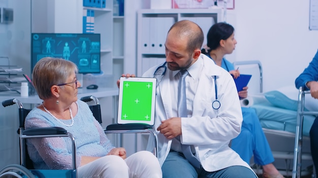 Praticante in possesso di tablet mock-up nel centro di recupero per pazienti anziani disabili. schermo verde chroma isolato facile sostituzione per app, testo, video o risorse digitali. medicina sanitaria e