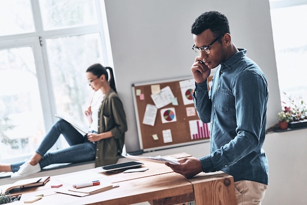 Praten met cliënt. Twee jonge moderne collega's in nette vrijetijdskleding die werken terwijl ze tijd doorbrengen in het creatieve kantoor