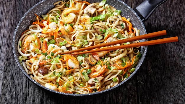 Prawn yaki udon stir fried udon noodles with shrimps cabbage\
chestnut mushrooms spring onion carrot mirin and soy sauce in a pan\
with chopsticks japan cuisine