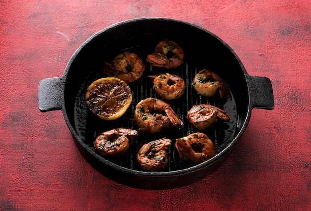 Prawns Shrimps roasted on frying grill pan with lemon  on a red concrete background