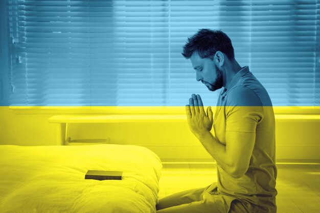 우크라이나를 위한 기도 방에서 기도하는 성경과 우크라이나 국기를 가진 남자의 이중 노출