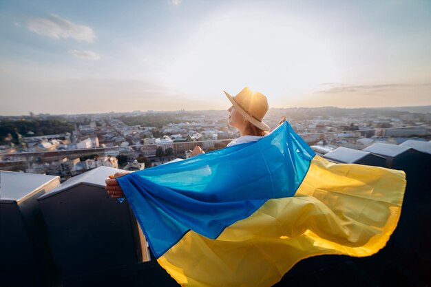 우크라이나를 위해 기도 xAA 여성은 우크라이나 국기와 함께 서서 우크라이나 국민의 독립과 힘의 LvivxAA 상징에서 일몰에 평화를 위해 그것을 흔들며 기도합니다