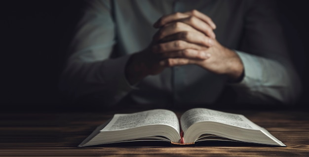 Рука человека молитвы на Библии в темной комнате