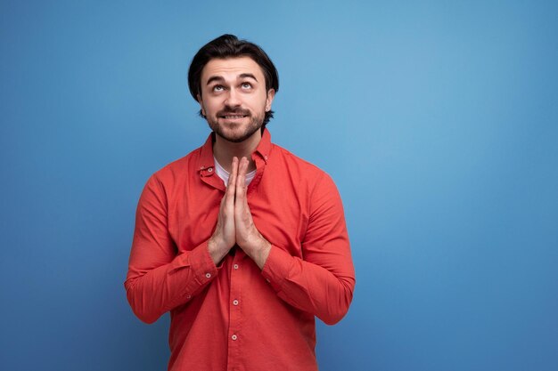 praying 35 year old brunette millennial man on a blue background with copy space