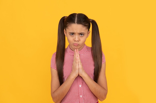 Praying girl child pray holding palms together in prayer gesture yellow background, plead.