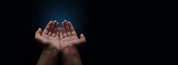 Praying hands with faith in religion and belief in God on dark background palm opening begging gesture panoramic layout