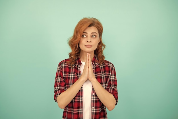 Praying redhead woman with curly hair in checkered casual shirt please