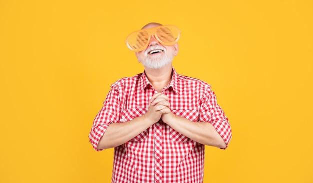 Photo praying senior man with party glasses on yellow background