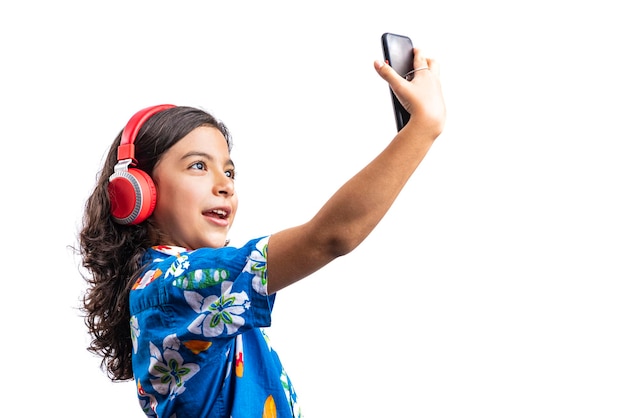 Pre latino teenager with a mobile phone and headphones taking a selfie on a white background