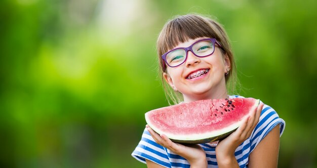 スイカのスライスを持っている庭の10代前の女の子幸せな女の子の子供がスイカを食べる女の子の子供...