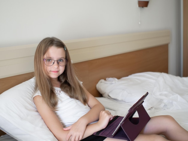 Photo pre teen girl with brown long hair siitting on sofa with tablet on the leg online studying concept