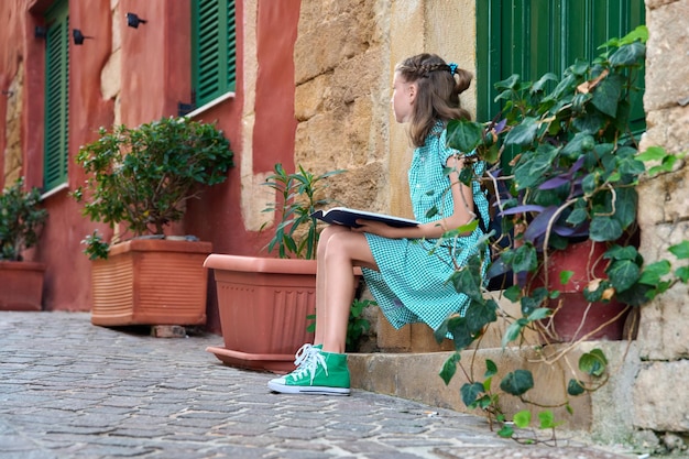 Preadolescent schoolgirl with a book sitting on steps of outdoor