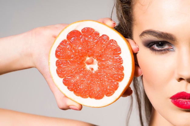 Photo preatty girl holding grapefruit cut in half next to the head
