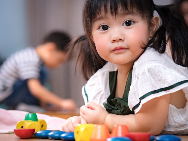 写真 2歳の健康的な愛らしいアジアの女の子の貴重な顔は、床に横になって、カラフルな木製モンテッソーリ感覚おもちゃを遊んでいます。かわいい幼児少女、最愛の娘、子どもの発達