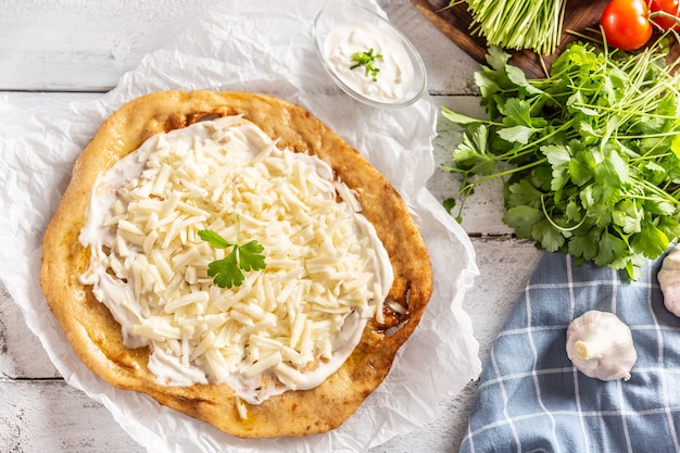 Precisely prepared hungarian traditional langos with lovely crust greased with garlic, cream, cheese and herbs, served with vegetables in the backround.