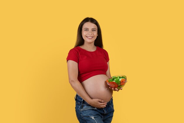 Pregnancy diet pregnant woman holding bowl with vegetable salad\
and embracing belly