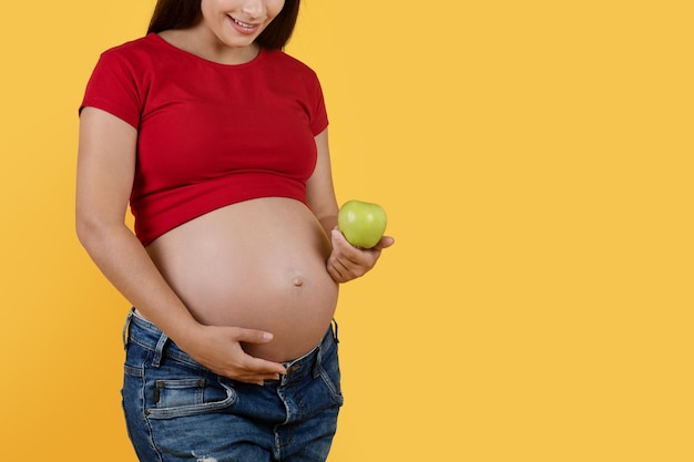 Pregnancy Diet Young pregnant female holding green apple and embracing her belly