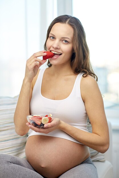 Photo pregnancy, food, healthy eating, people and expectation concept - happy pregnant woman eating fruits at home