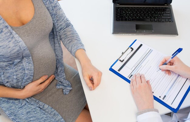 pregnancy, gynecology, medicine, health care and people concept - close up of gynecologist doctor with clipboard and pregnant woman meeting at hospital