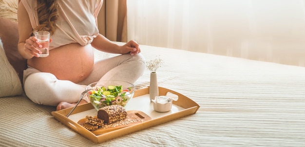 Pregnancy and healthy organic nutrition. Pregnant woman enjoying fresh vegetable salad in bed, free space