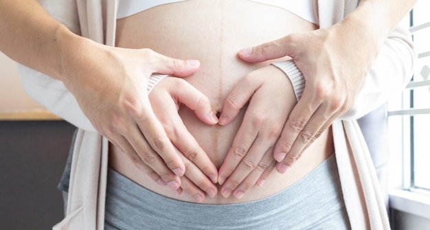 Foto concetto di amore per la gravidanza le mani dei genitori fanno il cuore sulla pancia