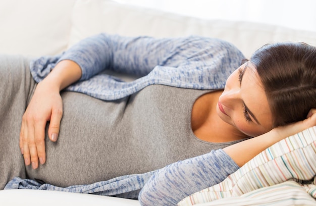 беременность, материнство, люди и концепция ожидания - крупный план счастливой беременной женщины с большим животом, лежащей дома на диване