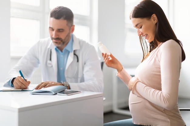 Pregnancy and medication concept Doctor prescribing pills for young pregnant woman during appointment in office