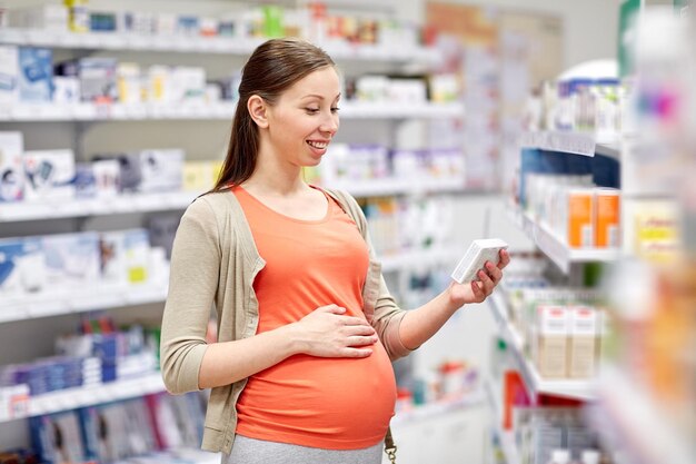 pregnancy, medicine, pharmaceutics, health care and people concept - happy pregnant woman with medication at pharmacy