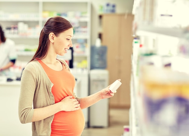 беременность, медицина, фармацевтика, здравоохранение и концепция людей - счастливая беременная женщина с лекарствами в аптеке