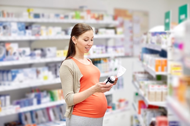 pregnancy, medicine, pharmaceutics, health care and people concept - happy pregnant woman with medication and prescription paper at pharmacy