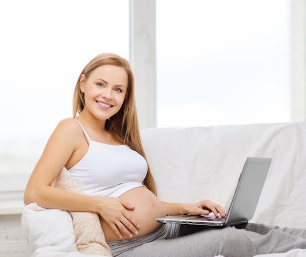 임신, 모성, 인터넷 및 기술 개념 - 노트북 컴퓨터와 함께 소파에 앉아 웃는 임산부