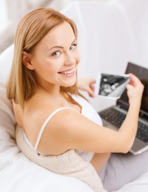 pregnancy, motherhood, medicine, health, internet and technology concept - smiling pregnant woman with laptop and ultrasound picture