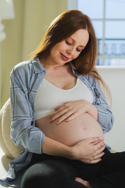 Pregnancy motherhood people expectation future pregnant woman touching big belly sitting on couch at