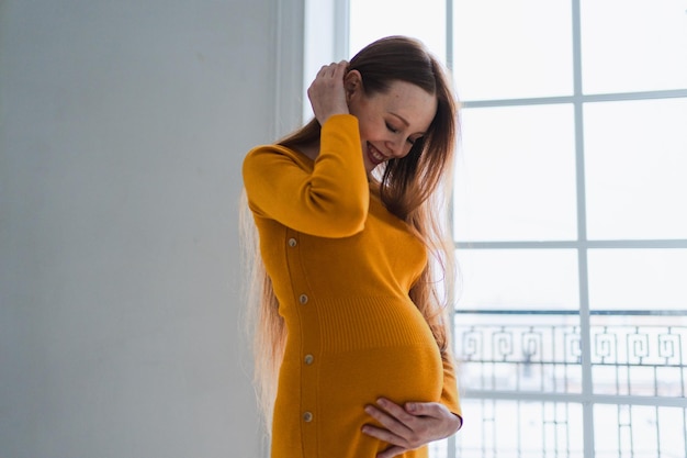 妊娠 母性 期待 将来の妊娠 腹の大きい女性が窓の近くに立っています