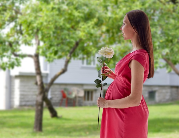 妊娠、母性、人、休日、期待のコンセプト – 家の庭や庭の背景に白いバラの花を持つ幸せな妊婦