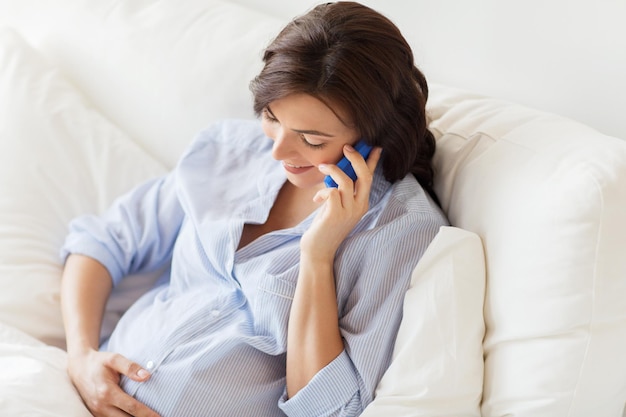 беременность, материнство, технологии, люди и концепция ожидания - счастливая беременная женщина звонит по смартфону в постели дома