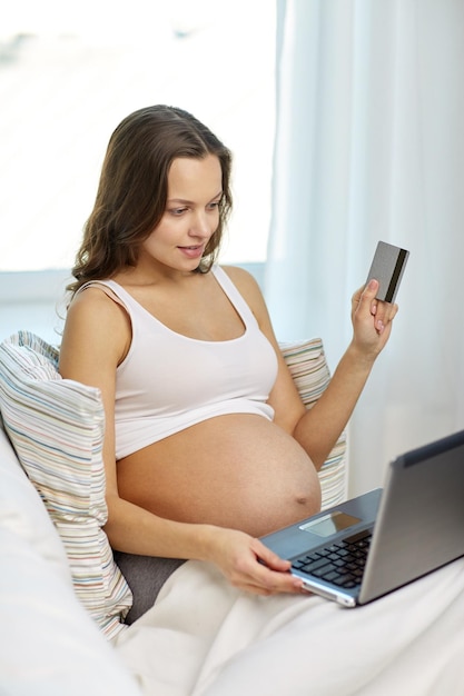 pregnancy, online shopping, technology and people concept - happy pregnant woman with laptop computer and credit card at home