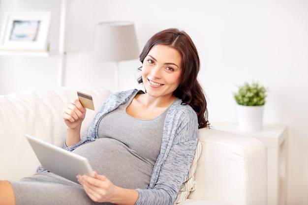 pregnancy, online shopping, technology and people concept - happy pregnant woman with tablet pc computer and credit card at home