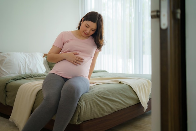 Беременность люди отдых и ожидание концепция азиатская улыбающаяся счастливая беременная женщина сидит в постели