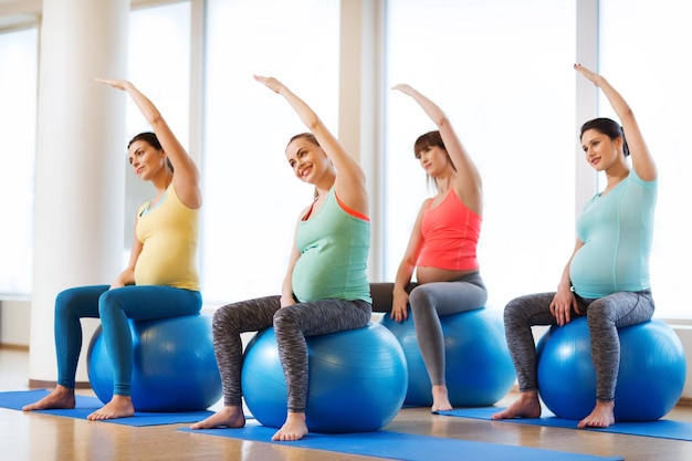 беременность, спорт, фитнес, люди и концепция здорового образа жизни - группа счастливых беременных женщин, тренирующихся на мяче в тренажерном зале