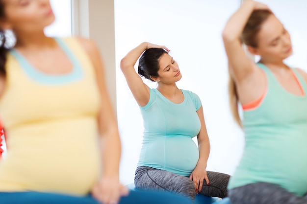 pregnancy, sport, fitness, people and healthy lifestyle concept - group of happy pregnant women exercising on ball in gym