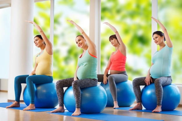 Pregnancy, sport, fitness, people and healthy lifestyle concept - group of happy pregnant women exercising on ball in gym